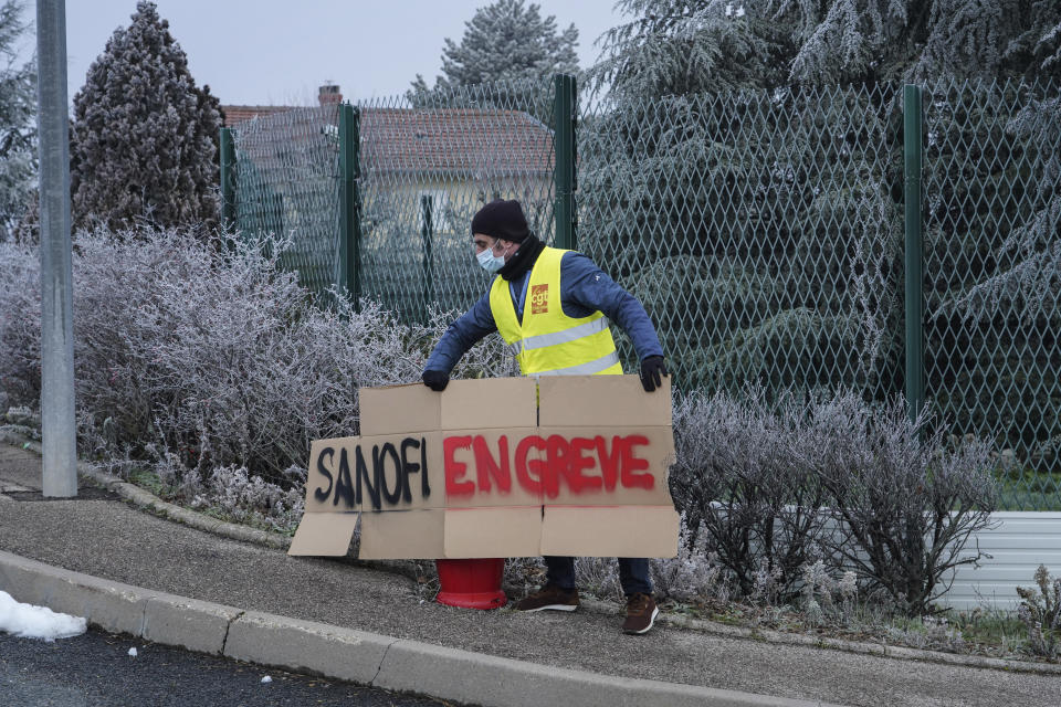 A worker install a poster reading "Sanofi on strike" outside the French pharmaceutical company Sanofi headquarters in Marcy l'Etoile, central France, Tuesday, Jan.19, 2021. Employees of pharmaceutical company Sanofi stage a protest against planned redundancies that they say could slow the fight against the Coronavirus pandemic . Sanofi had been developing Covid vaccines but will not be ready to roll out until late 2021. (AP Photo/Laurent Cipriani)