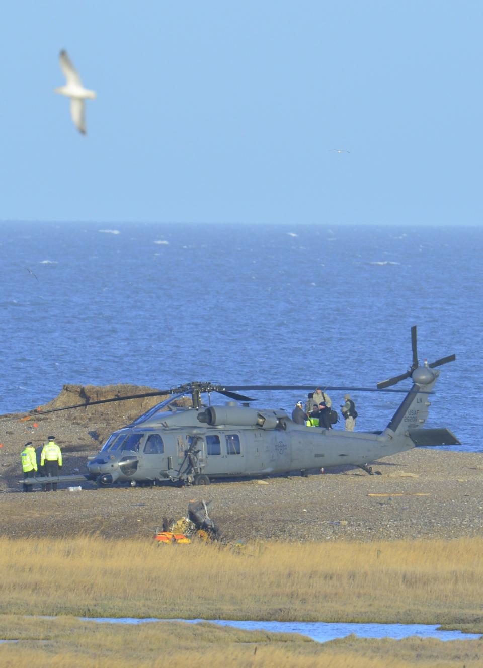 A Pave Hawk helicopter, military personnel and emergency services attend the scene of a helicopter crash on the coast near the village of Cley in Norfolk, eastern England