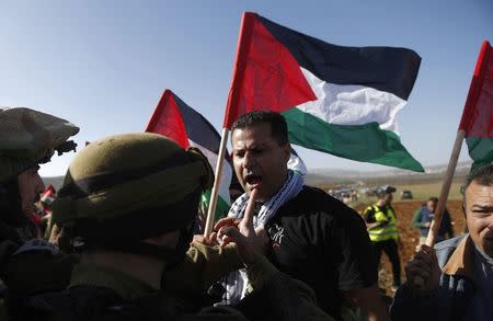 A Palestinian protester holds a Palestinian flag as he argues with Israeli soldiers during a protest against Jewish settlements near the West Bank city of Ramallah December 10, 2014. REUTERS/Mohamad Torokman