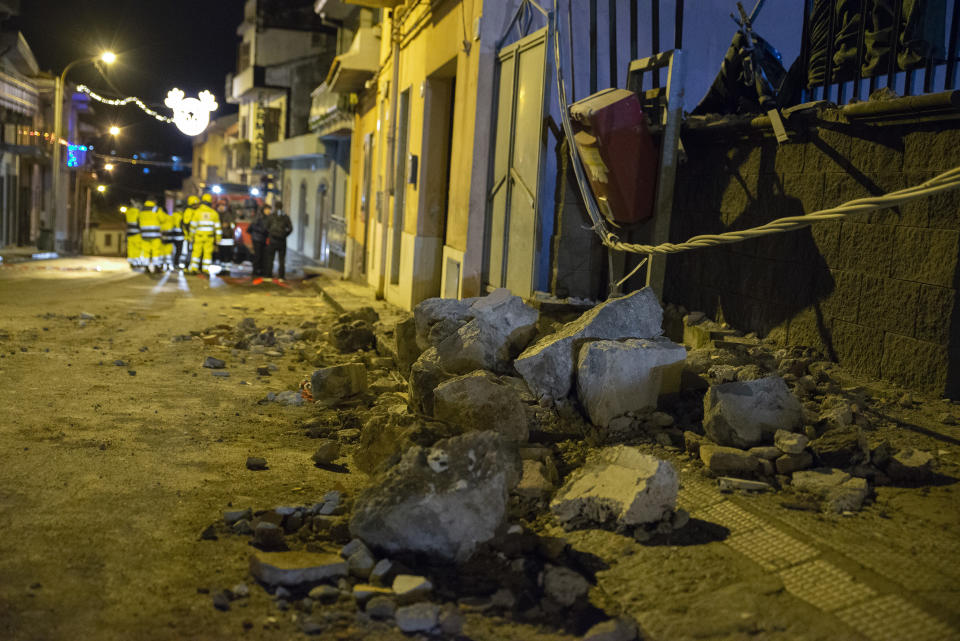 Debris of a damaged house sit on a street as Italian Civil Protection volunteers, seen on background, gather in Fleri, Sicily Italy, Wednesday, Dec. 26, 2018. A quake triggered by Italy's Mount Etna volcano has jolted eastern Sicily, slightly injuring 10 people and prompting frightened Italian villagers to flee their homes. (AP Photo/Salvatore Allegra)
