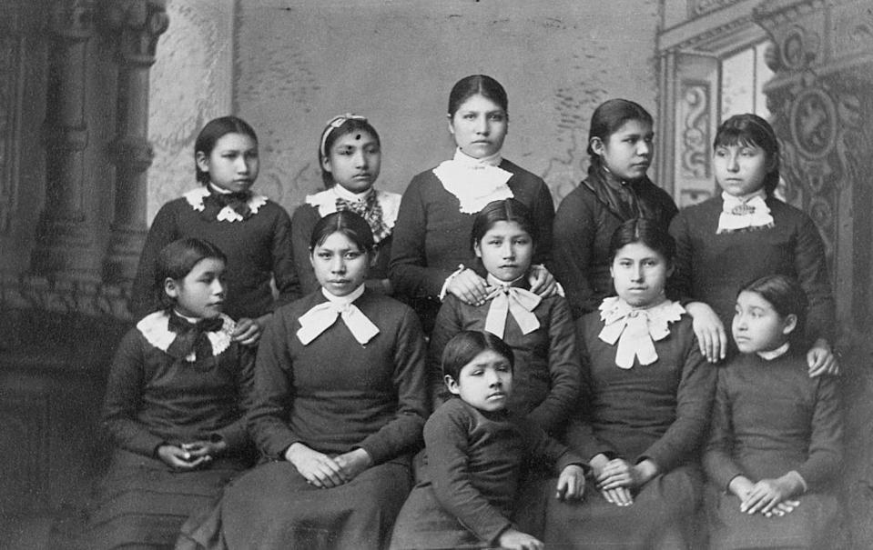 A black and white photo shows two rows of girls in black dresses with white collars.