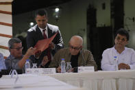 Pablo Beltran, of of the Colombian guerrilla National Liberation Army (ELN), receives documents to sign, next to ELN member Antonio Garcia, center, as they sit with Colombian government representative Ivan Danilo Rueda during a signing ceremony agreeing to resume peace talks, at the Casa Cultural Aquiles Nazoa in Caracas, Venezuela, Tuesday, Oct. 4, 2022. The agreement comes after more than four years of suspension, and will start in November. (AP Photo/Ariana Cubillos)