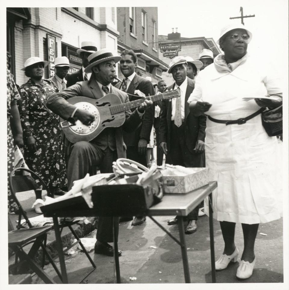 A man plays a guitar and is surrounded by a crowd during the Big Quarterly in Wilmington, Delaware in 1939.