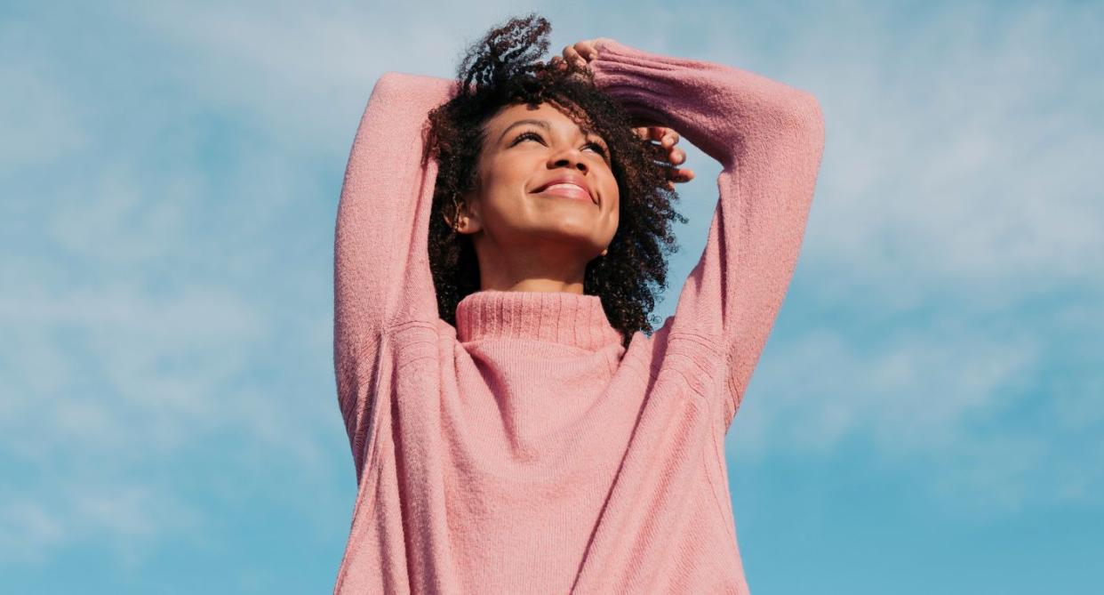 Happy woman smiling pink jumper blue skies. (Getty Images)