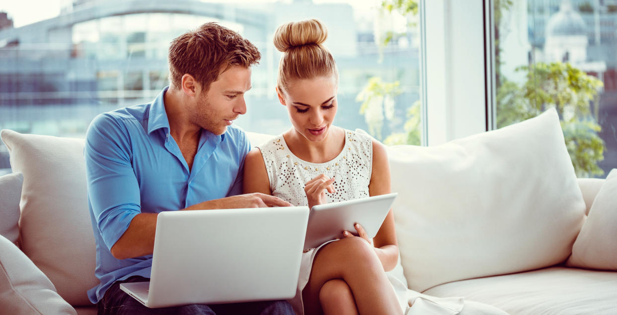 couple on couch looking at laptop tablet