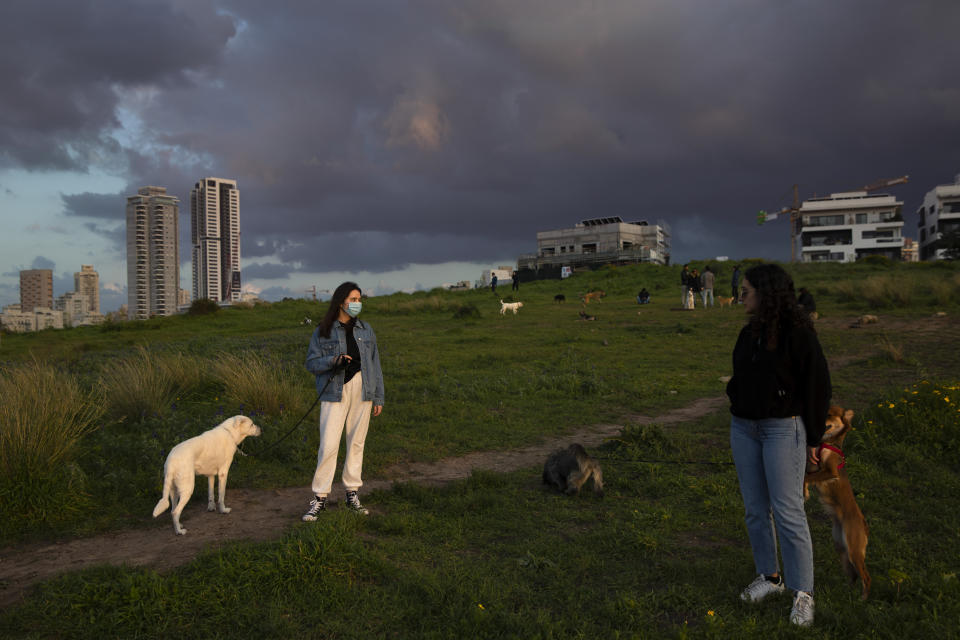 A woman wears a face mask as she walks her dog at a park in Tel Aviv, Israel, Wednesday, March 18, 2020. Israel braced for its first fatalities as the number of coronavirus cases spiked by 25% on Wednesday. For most people, the virus causes only mild or moderate symptoms. For some it can cause more severe illness. (AP Photo/Oded Balilty)