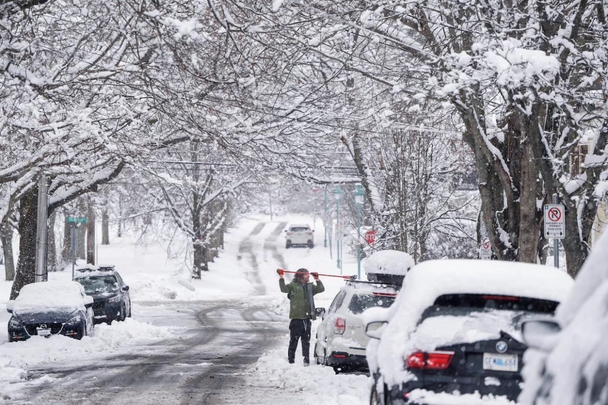 A person uses a broom to clean snow from their vehicle following the first significant snowfall of the season in Halifax in December.  (Darren Calabrese/The Canadian Press - image credit)