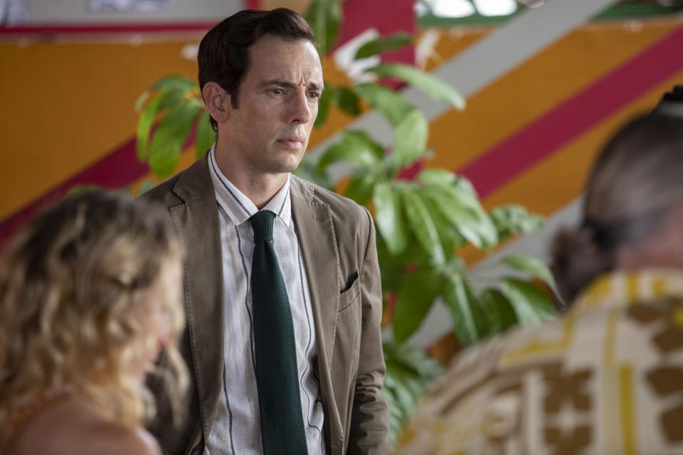 Neville (Ralf Little) stands in front of the suspects — we can see Petra (Leah Brotherhead) and Ivan (Pearce Quigley) in the foreground with their backs to the camera