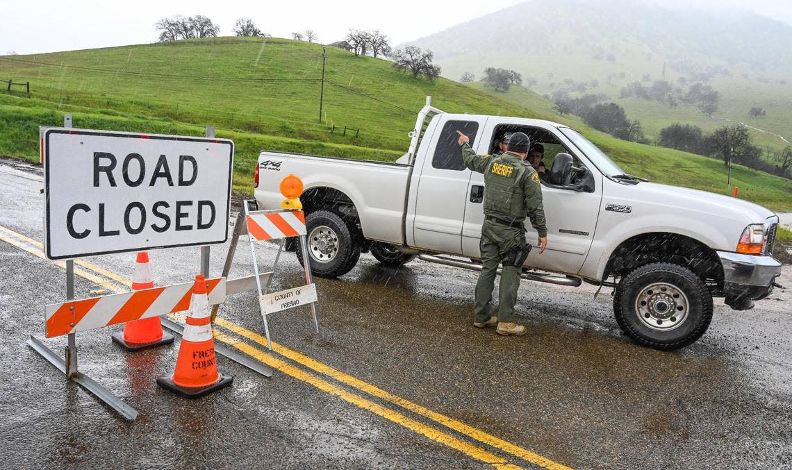 A Fresno County Sheriff deputy gives information to a resident at a roadblock at Elwood Road and Piedra Road in eastern Fresno County on Friday, March 10, 2023. The road was closed due to being washed out in heavy rain and runoff.