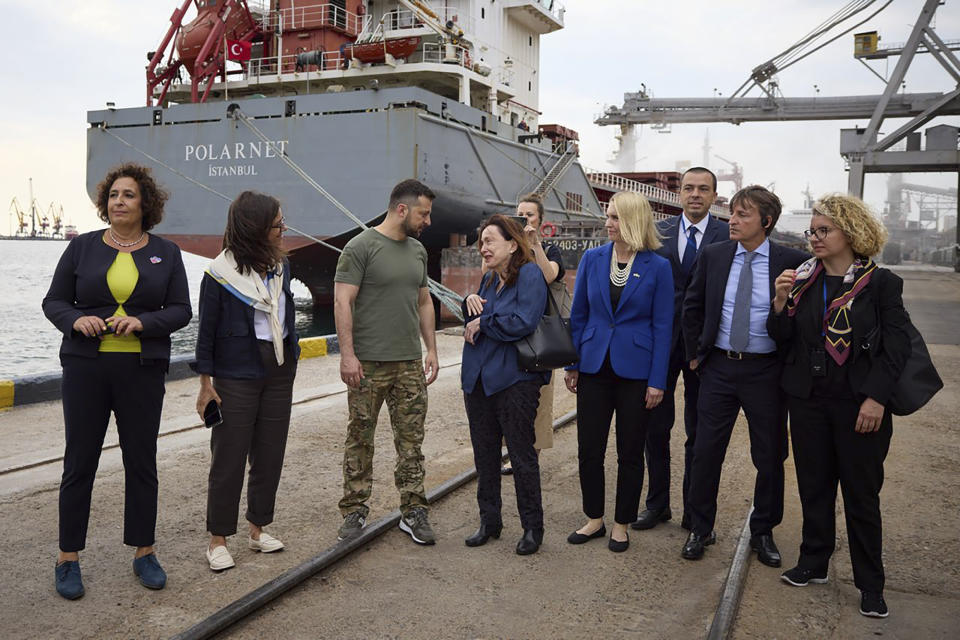 In this photo provided by the Ukrainian Presidential Press Office, Ukrainian President Volodymyr Zelenskyy, center, surrounded by ambassadors of different countries and UN officials, visits a port in Chornomork during loading of grain on a Turkish ship, background, close to Odesa, Ukraine, Friday, July 29, 2022. (Ukrainian Presidential Press Office via AP)