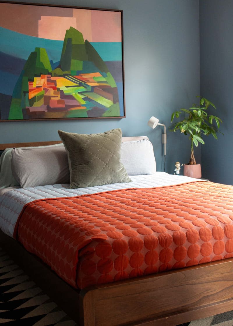 Orange blanket on neatly made bed in blue painted bedroom.