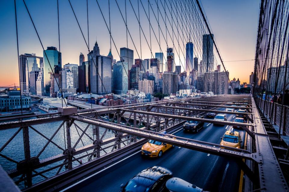 Cars drive across the Brooklyn Bridge in Manhattan at dusk