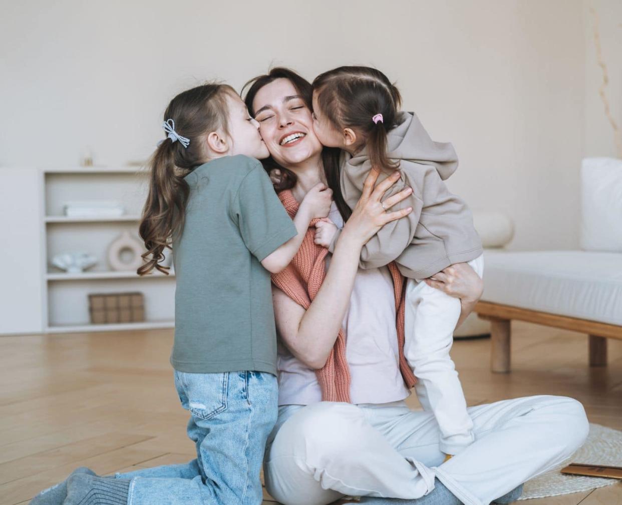mother's day: mom being hugged and kissed by two daughters - Motherly says mothering is work