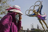 FILE - In this May 2, 2021, file photo, a woman adjusts her face mask as she walks by a statue featuring the Beijing Winter Olympics figure skating on display at the Shougang Park in Beijing. China's "zero tolerance" strategy of trying to isolate every case and stop transmission of the coronavirus has kept kept the country where the virus first was detected in late 2019 largely free of the disease. (AP Photo/Andy Wong, File)