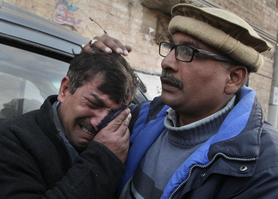 A man comforts a relative of Christian priest Father William Siraj, 75, who was killed by unknown gunmen, mourn next to his body at his home in Peshawar, Pakistan, Sunday, Jan. 30, 2022. Police said gunmen killed Siraj and wounded another priest as they were driving home from Sunday Mass in Pakistan’s northwestern city of Peshawar. (AP Photo/Muhammad Sajjad)