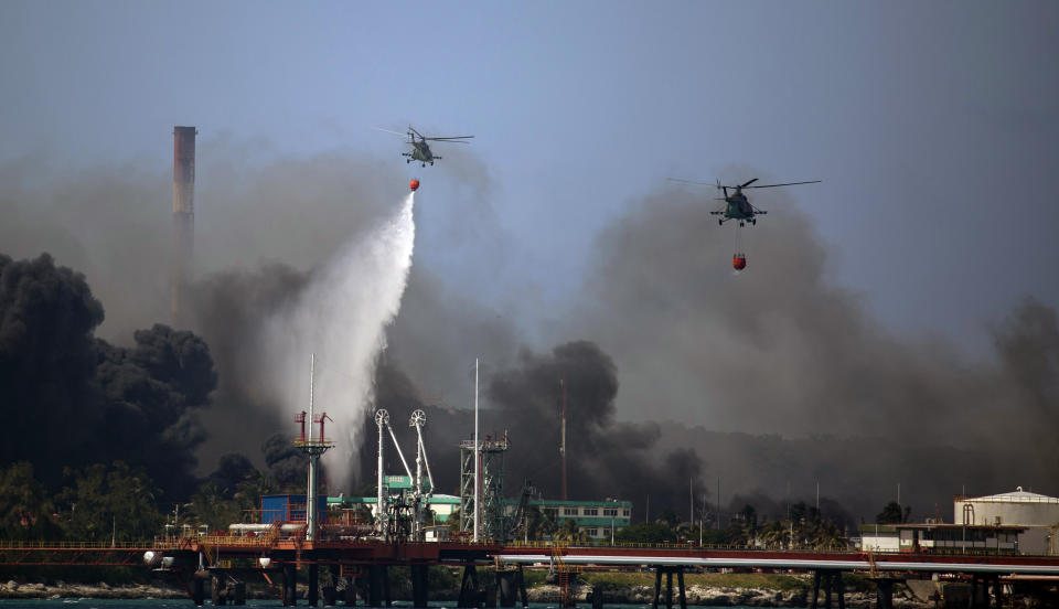 Helicopters hauling water fly over the Matanzas Supertanker Base, as firefighters and specialists work to quell the blaze which began during a thunderstorm in Matanzas, Cuba, Monday, Aug. 8, 2022. Cuban authorities say lightning struck a crude oil storage tank at the base, sparking a fire that sparked four explosions. (AP Photo/Ismael Francisco)