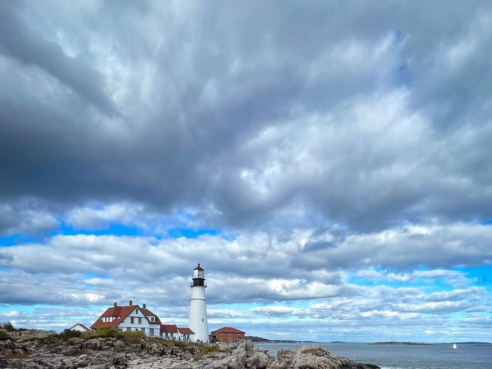 Emily sits on a rocky coastline with a lighthouse in the background.