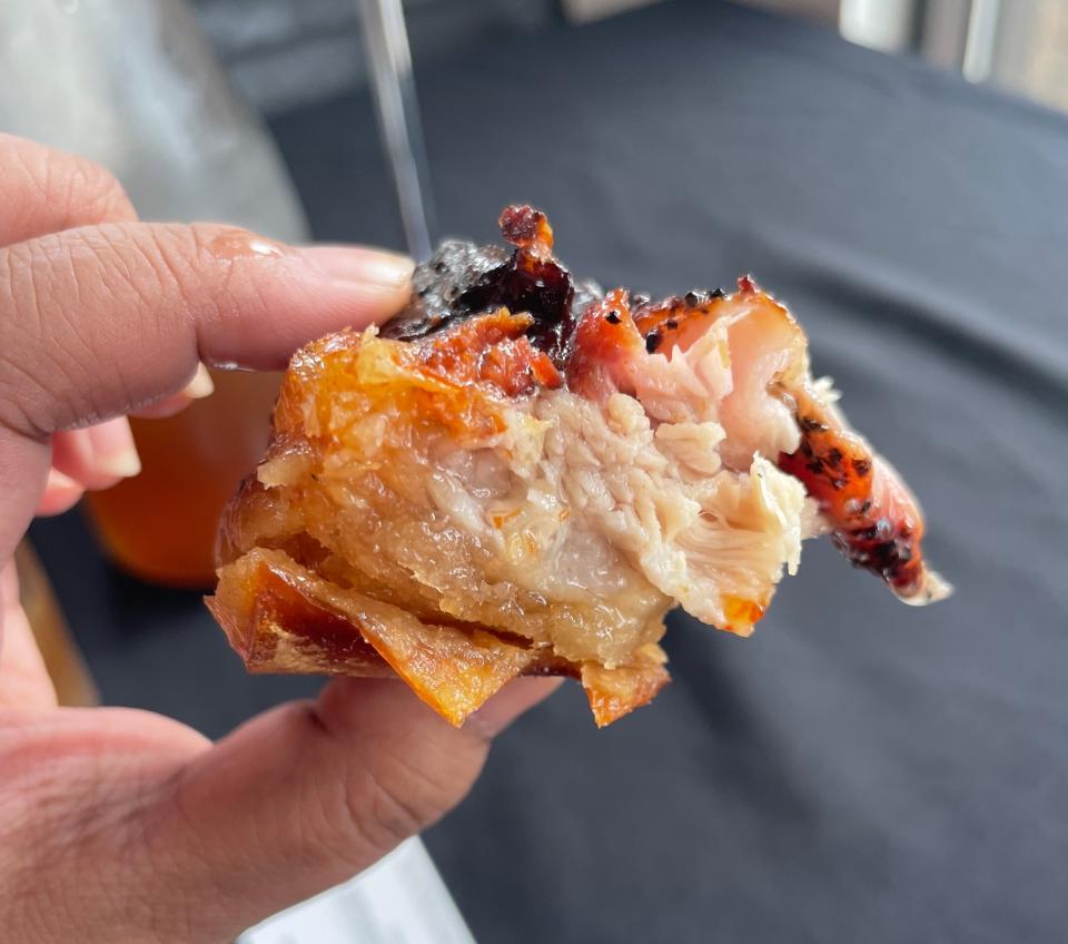 A person holds a piece of roasted pig, showing its juicy and tender texture with a crispy, charred skin