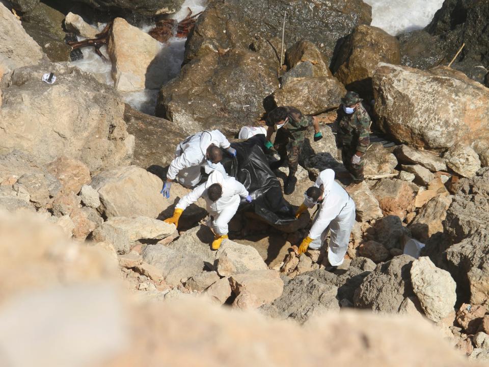 A rescue team in white suits cary a body bag up from the rocky shore of Derna.