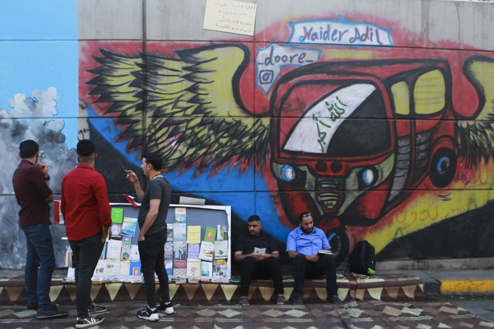 In this Sunday, Nov. 17, 2019 photo, protesters read donated books in front of graffiti, at the Saadoun Tunnel, in Baghdad, Iraq. The tunnel that passes under Baghdad’s landmark Tahrir Square has become an ad hoc museum for Iraq's revolution: Young artists draw images and murals that illustrate the country’s tortured past, and the Iraq they aspire to. (AP Photo/Hadi Mizban)