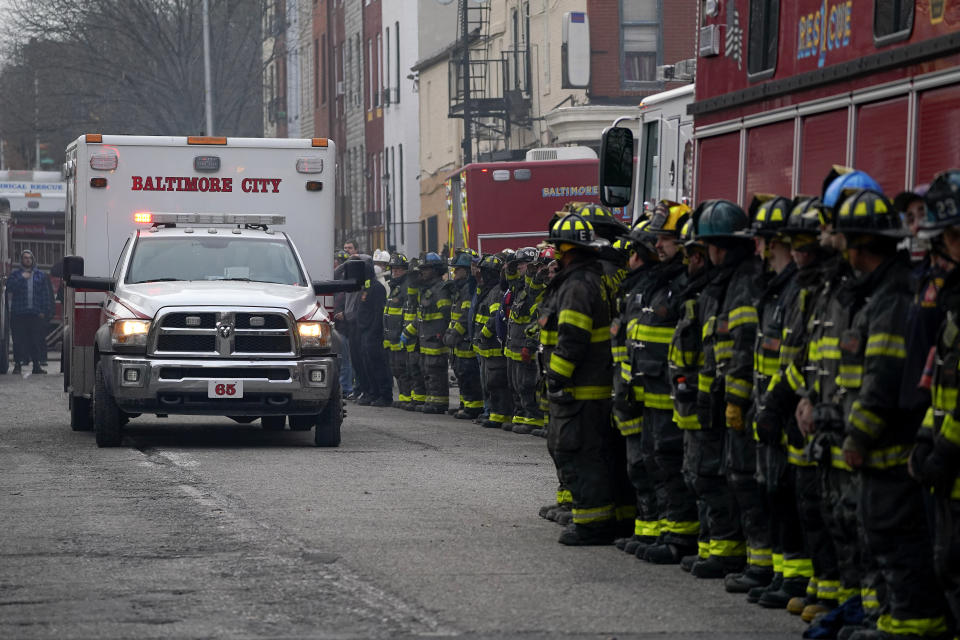 Firefighters salute as an ambulance carries a deceased firefighter after they were pulled out of a collapsed building while battling a two-alarm fire at a vacant row home, Monday, Jan. 24, 2022, in Baltimore. Officials said several firefighters died during the blaze. (AP Photo/Julio Cortez)