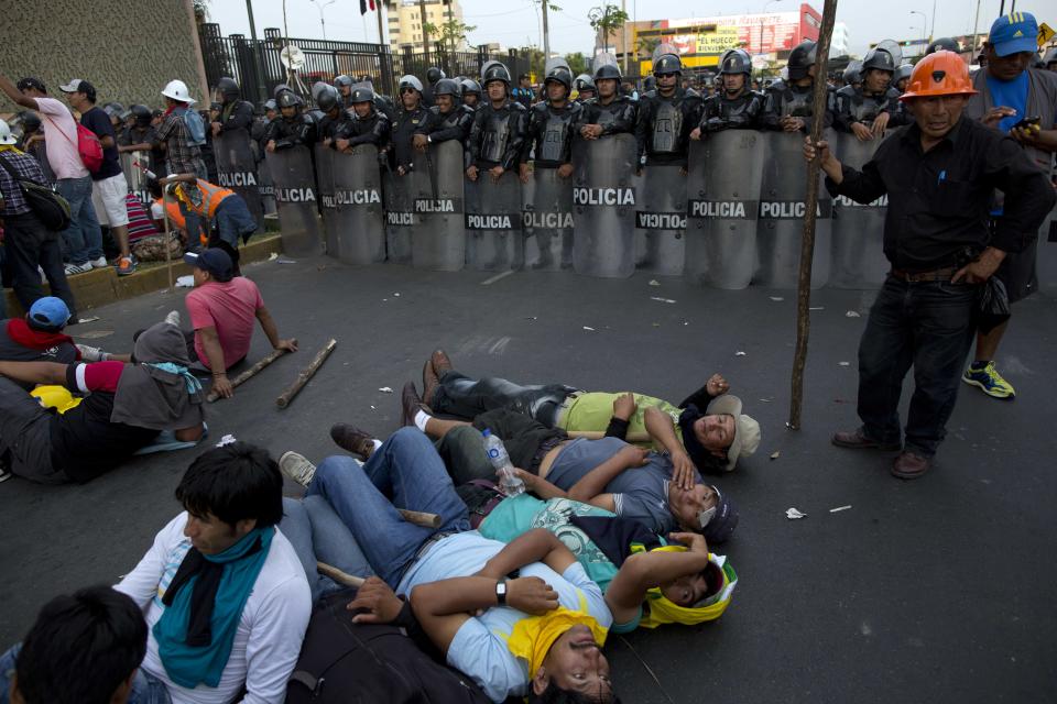 Varios mineros acostados en el suelo cerca de la policía antimotines durante una protesta organizada por mineros artesanales de oro en Lima, Perú, el lunes 24 de marzo de 2014. Los mineros marcharon por la capital por quinto día consecutivo para pedir al gobierno que eche atrás nuevas normas que los obligan a regularizarse. (Foto AP/Rodrigo Abd)