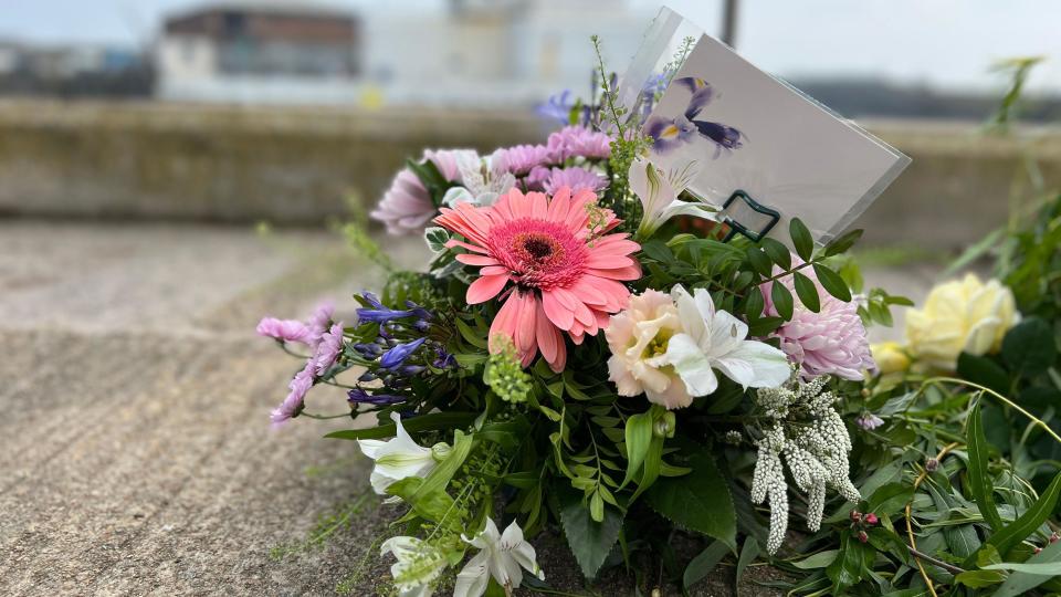 A boquet of flowers is on the ground of the pier with a card placed inside 