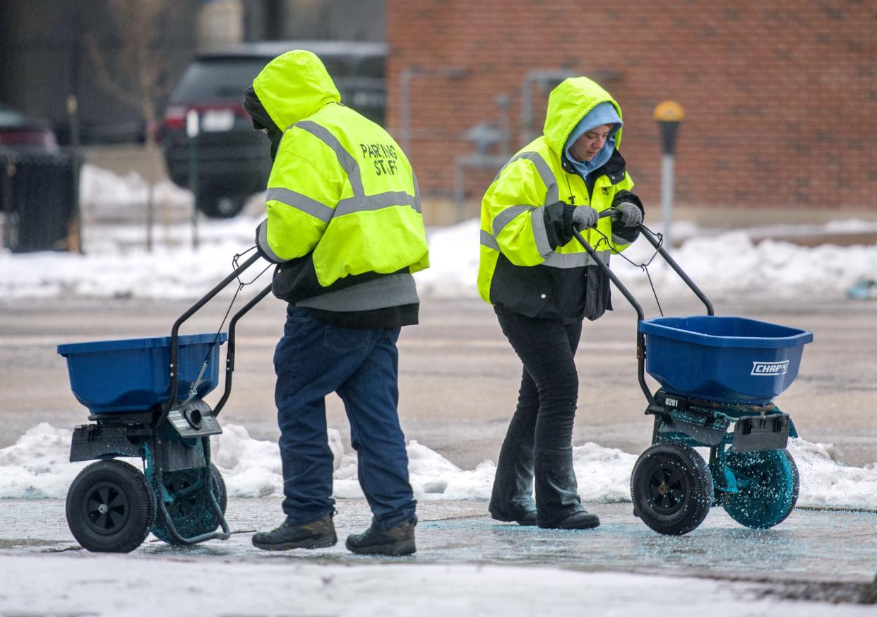 A pair of Heartland Parking attendants team up to salt the icy sidewalks Monday, Jan. 22, 2024 around the PNC Bank parking deck along Harrison Street in downtown Peoria.