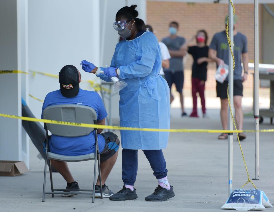 Health care workers take throat swabs on residents who wanted to be tested for the coronavirus outside the Duval County Health Department on July 28 in Jacksonville, Fla. As the number of people infected by the COVID-19 virus spikes, the department has stayed busy with long lines of residents waiting for tests and  vaccines.