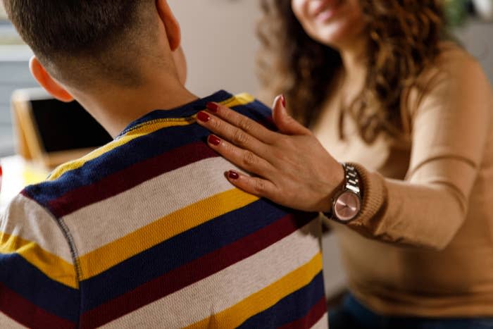 A mom placing a comforting hand on her teenage son's shoulder