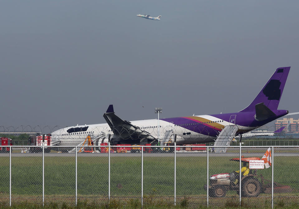 An airport worker drives a cart by a damaged Thai Airways Airbus A330-300 as a passenger planer takes off at Sunvarnabhumi International Airport in Bangkok, Thailand Monday, Sept. 9, 2013. The plane carrying more than 280 people skidded off the runway while landing Sunday, injuring 14 passengers. After the accident, workers on a crane blacked out the Thai Airways logo on the tail and body of the aircraft. (AP Photo/Apichart Weerawong)