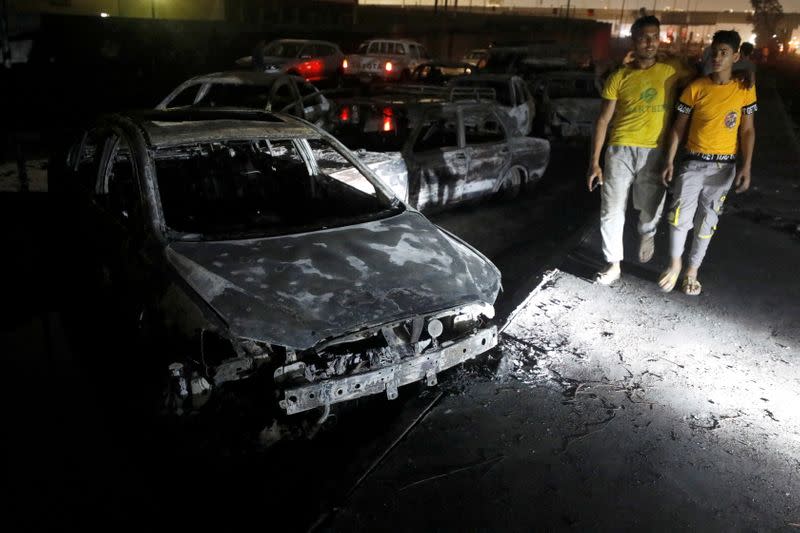 People walk past burned vehicles following a fire that broke out in Egypt's Shuqair-Mostorod crude oil pipeline, at the beginning of Cairo-Ismailia road