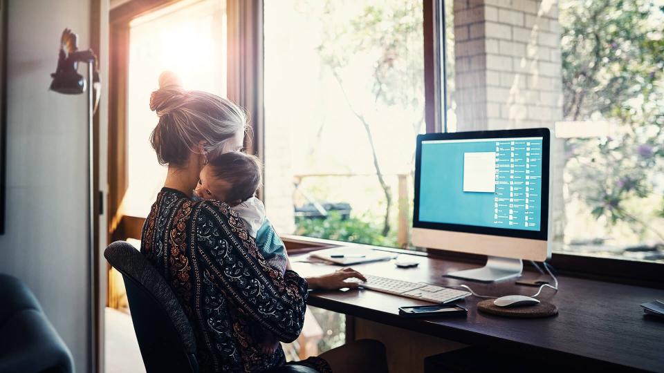 young woman working at home while holding her newborn baby son