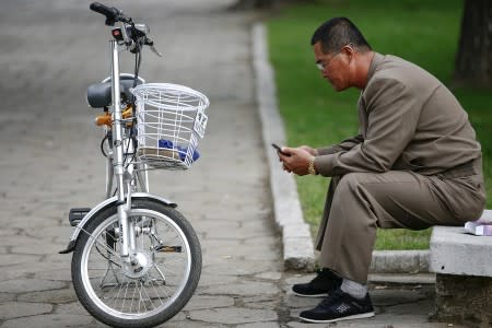 FILE PHOTO : A man uses his mobile phone next to an electric bicycle in downtown Pyongyang