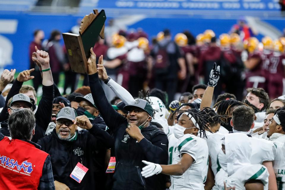 West Bloomfield head coach Ron Bellamy holds the trophy and celebrates with players and coaches after defeating Davison, 41-0, in the MHSAA Division 1 final at Ford Field, Saturday, Jan. 23, 2021.