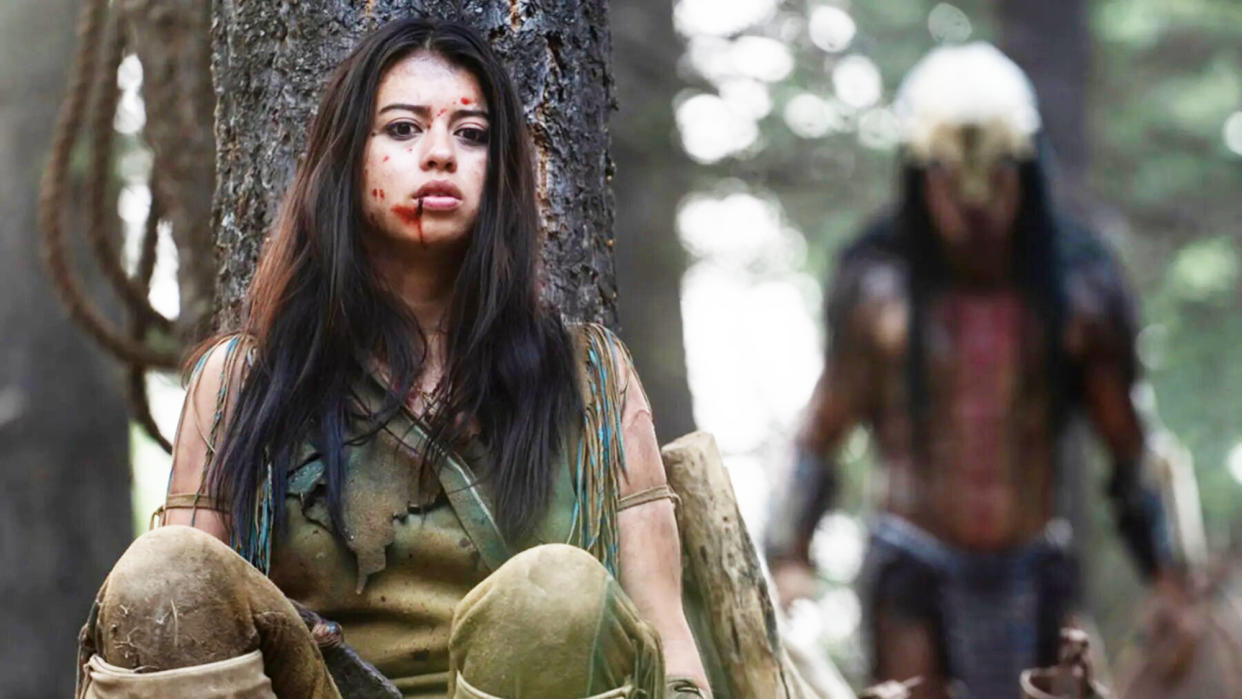  Amber Midthunder as Naru, hiding behind a tree with the Predator behind her in Prey movie on Disney Plus. 
