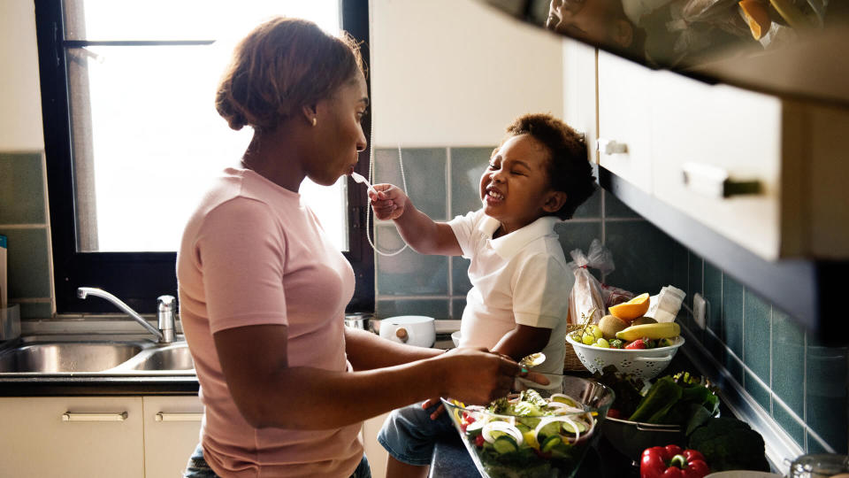 Black kid feeding mother with cooking food in the kitchen.