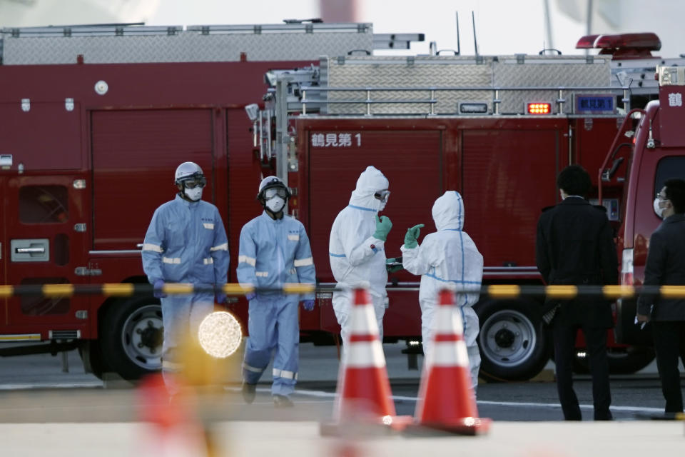 Officials wearing protective suits stand near the cruise ship Diamond Princess at Yokohama Port in Yokohama, south of Tokyo, Thursday, Feb. 6, 2020. Health workers said 10 more people from the Diamond Princess were confirmed ill with the virus, in addition to 10 others who tested positive on Wednesday. They were dropped off as the ship docked and transferred to nearby hospitals for further test and treatment. (AP Photo/Eugene Hoshiko)