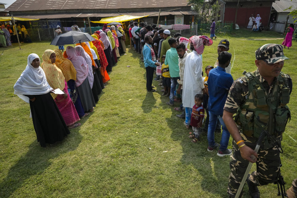 A security person walks past queues of voters in a polling station on the bank of the Brahmaputra river during the second round of voting in the six-week-long national election in Morigaon district, Assam, India, Friday, April 26, 2024. (AP Photo/Anupam Nath)