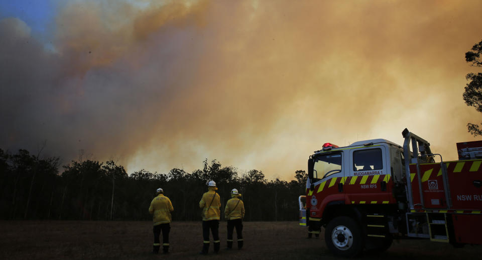 NSW firefighters are seen here at a property at Old Bar as a bushfire burns. A state of emergency has been declared.
