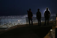 Residents stand on a hill before barriers, wrapped in concertina wire, separating Mexico and the United States, where the border meets the Pacific Ocean, in Tijuana, Mexico, Saturday, Nov. 17, 2018. Many of the nearly 3,000 migrants have reached the border with California. The mayor has called the migrants' arrival an "avalanche" that the city is ill-prepared to handle. (AP Photo/Marco Ugarte)