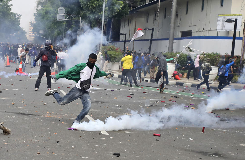 A student protester kicks a tear gas canister fired by police during a rally against a controversial bill on job creation in Jakarta, Indonesia, Thursday, Oct. 8, 2020. Thousands of enraged students and workers staged rallies across Indonesia on Thursday in opposition to the new law they say will cripple labor rights and harm the environment. (AP Photo/Dita Alangkara)