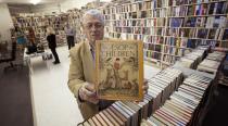 In this Friday, Oct. 19, 2012 photo, memorabilia collector Ken Kallin displays one of his antique books that will be sold at auction in Oakland Park, Fla. Three decades ago, Kallin began amassing 120,000 pieces in a memorabilia collection that includes photographs signed by Muhammad Ali and Neil Armstrong along with rare books and trading cards. By the end of Saturday, Oct. 27, 2012 he's hoping to have gotten rid of nearly all of it _ at an auction to benefit his daughter, who suffers from a rare autoimmune disease that makes her bones dangerously brittle and causes her body's defenses to attack her own blood vessels. (AP Photo/J Pat Carter)