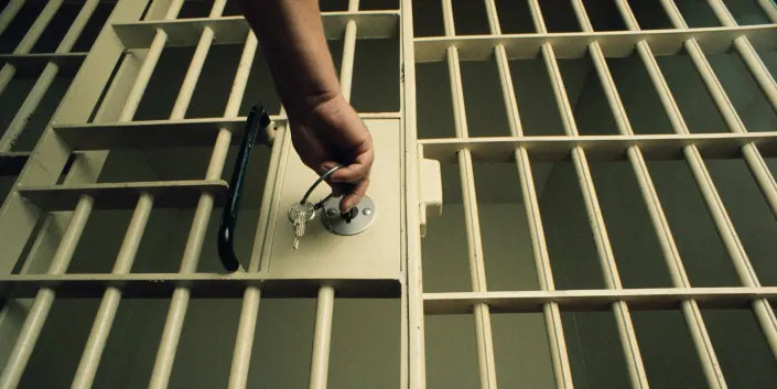 A stock image of a hand putting a key in a jail cell door, viewed from below.