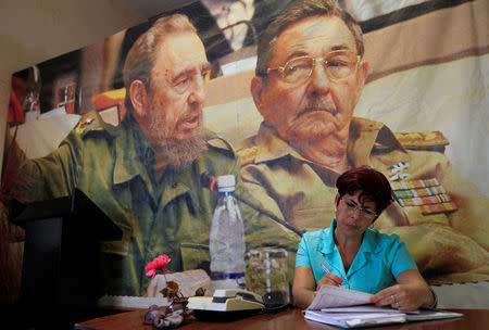 A woman works under a picture of Cuba's former president Fidel Castro (L) and his brother and Cuba's president Raul Castro in Artemisa province, Cuba November 27, 2016. REUTERS/Enrique de la Osa