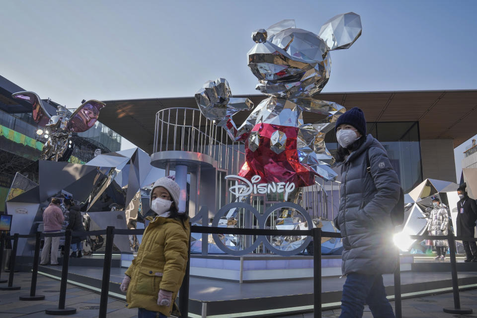 A woman and a child wearing face masks walk by a Mickey Mouse statue on display at an outdoor shopping center commemorating Disney 100th anniversary, in Beijing, Thursday, Jan. 5, 2023. As COVID-19 rips through China, other countries and the WHO are calling on its government to share more comprehensive data on the outbreak, with some even saying many of the numbers it is reporting are meaningless. (AP Photo/Andy Wong)