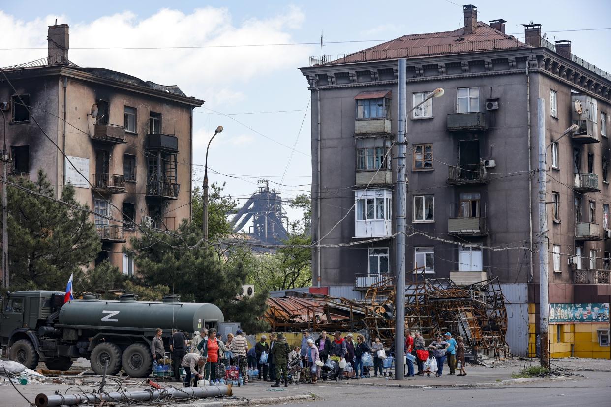 FILE - Local civilians gather to receive pure water distributed by Russian Emergency Situations Ministry in Mariupol, in territory under the government of the Donetsk People's Republic, eastern Ukraine, on May 27, 2022, with the Illich Iron & Steel Works Metallurgical Plant is in the background. According to Russian state TV, the future of the Ukrainian regions occupied by Moscow's forces is all but decided: Referendums on becoming part of Russia will soon take place there, and the joyful residents who were abandoned by Kyiv will be able to prosper in peace. In reality, the Kremlin appears to be in no rush to seal the deal on Ukraine's southern regions of Kherson and Zaporizhzhia and the eastern provinces of Donetsk and Luhansk. (AP Photo/Alexei Alexandrov)