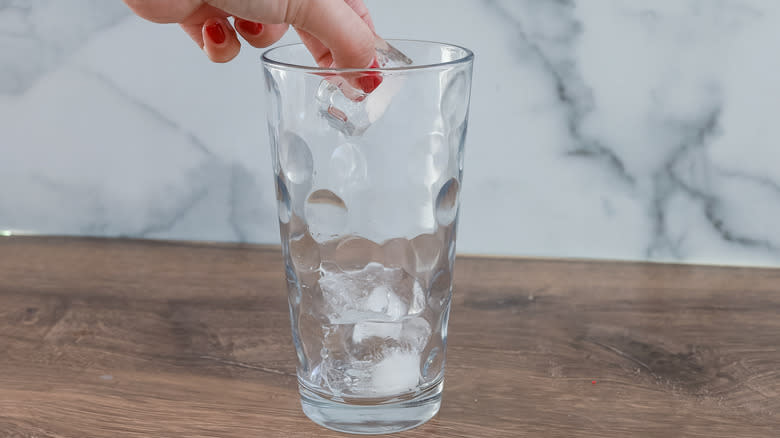 Hand adding ice to glass