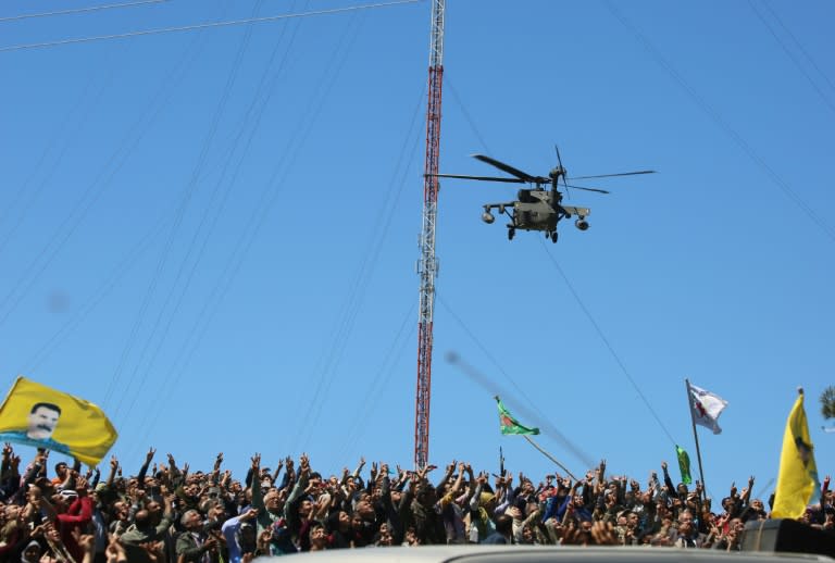 Kurds wave flags as a medevac helicopter from the US-led coalition flies over the site of Turkish air strikes near Al-Malikiyah on April 25, 2017