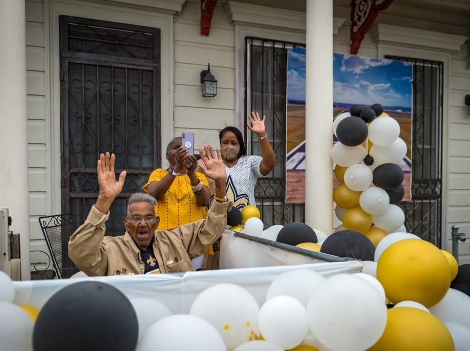 Lawrence Brooks raises his hands above his head and smiles as he celebrates his 112th birthday on his front porch, surrounded by white, black, and gold balloons.